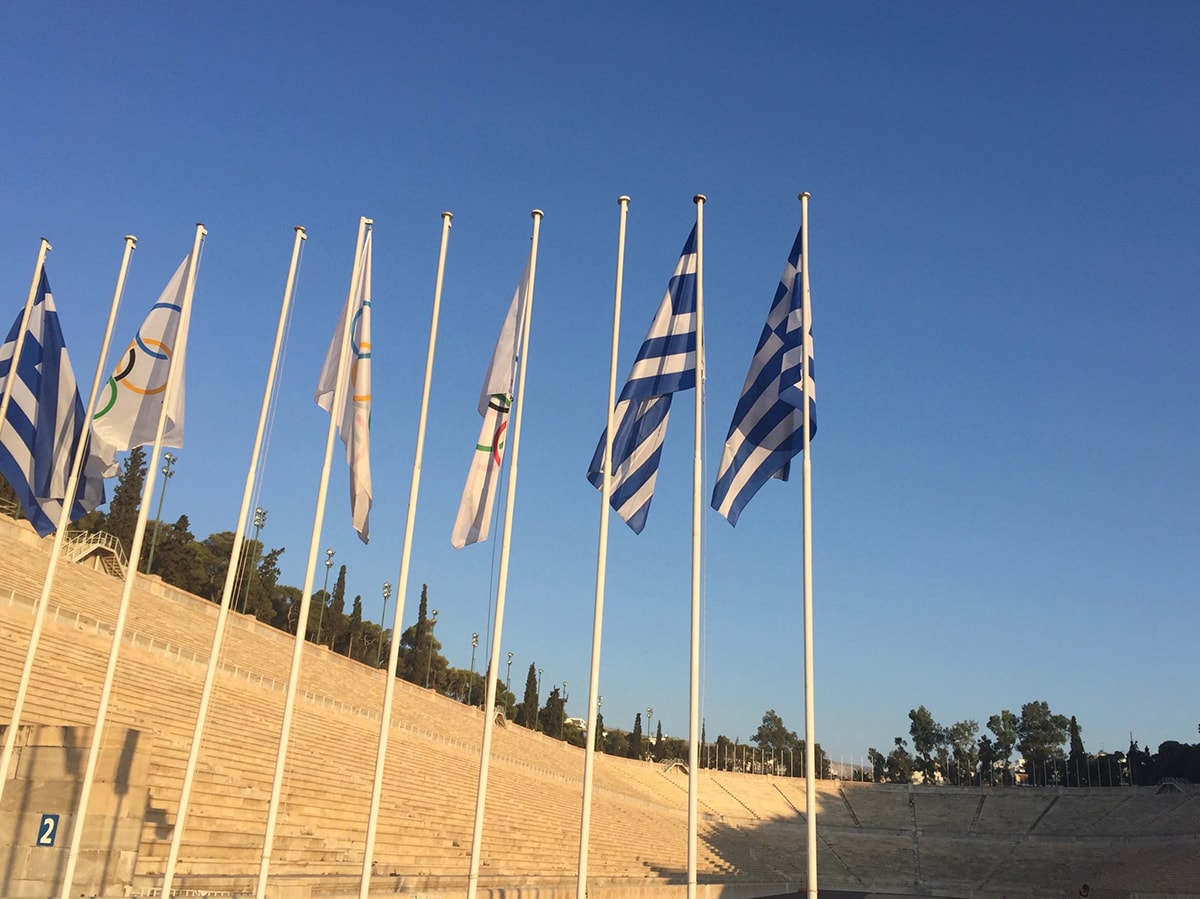 Olympic and Greek flags hang in the foreground of the Panathenaic Stadium in Athens, Greece